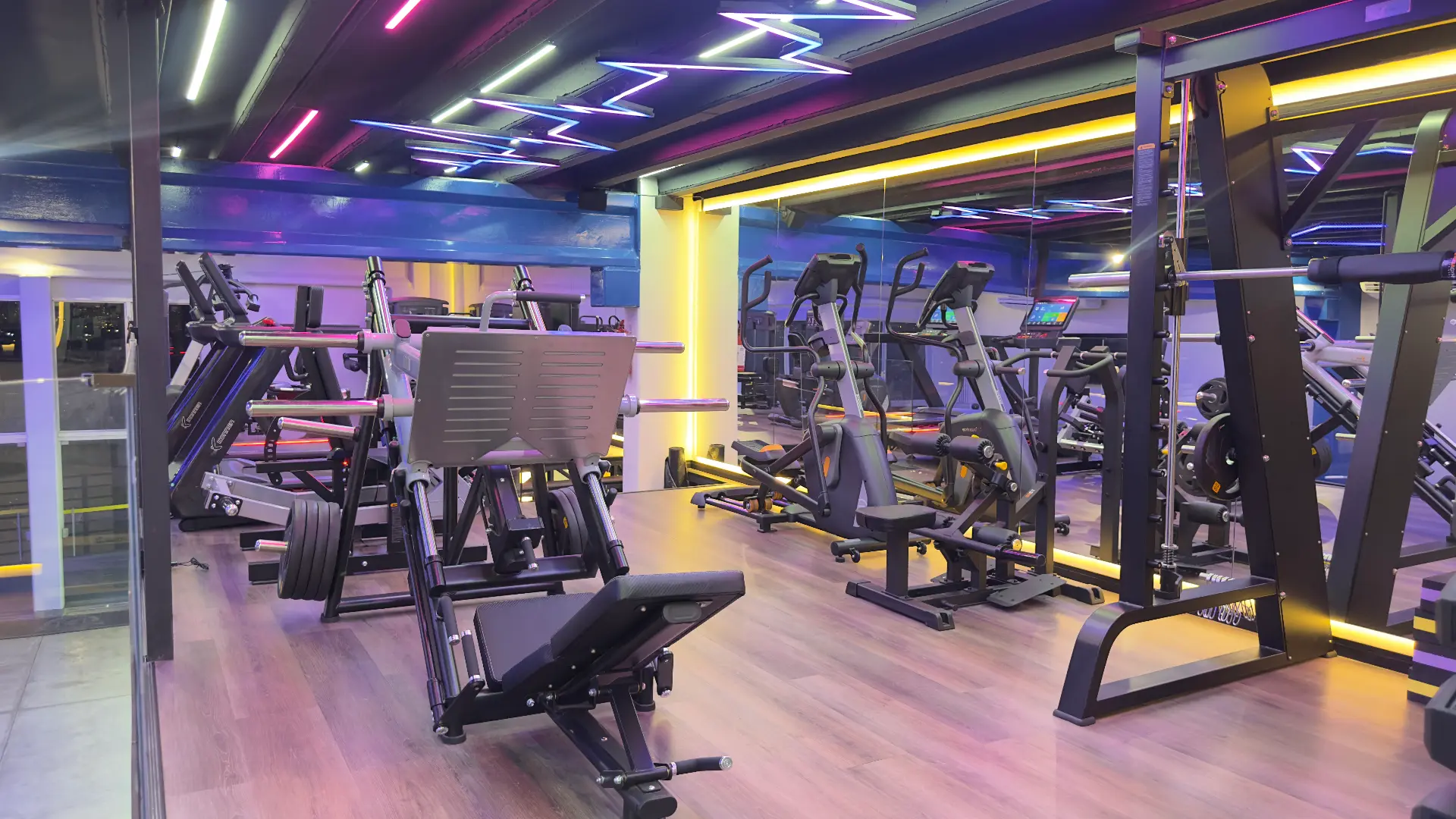 Área de leg press, elípticos e esteiras da Sumrak 408 com piso em madeira e espelhos de parede inteira